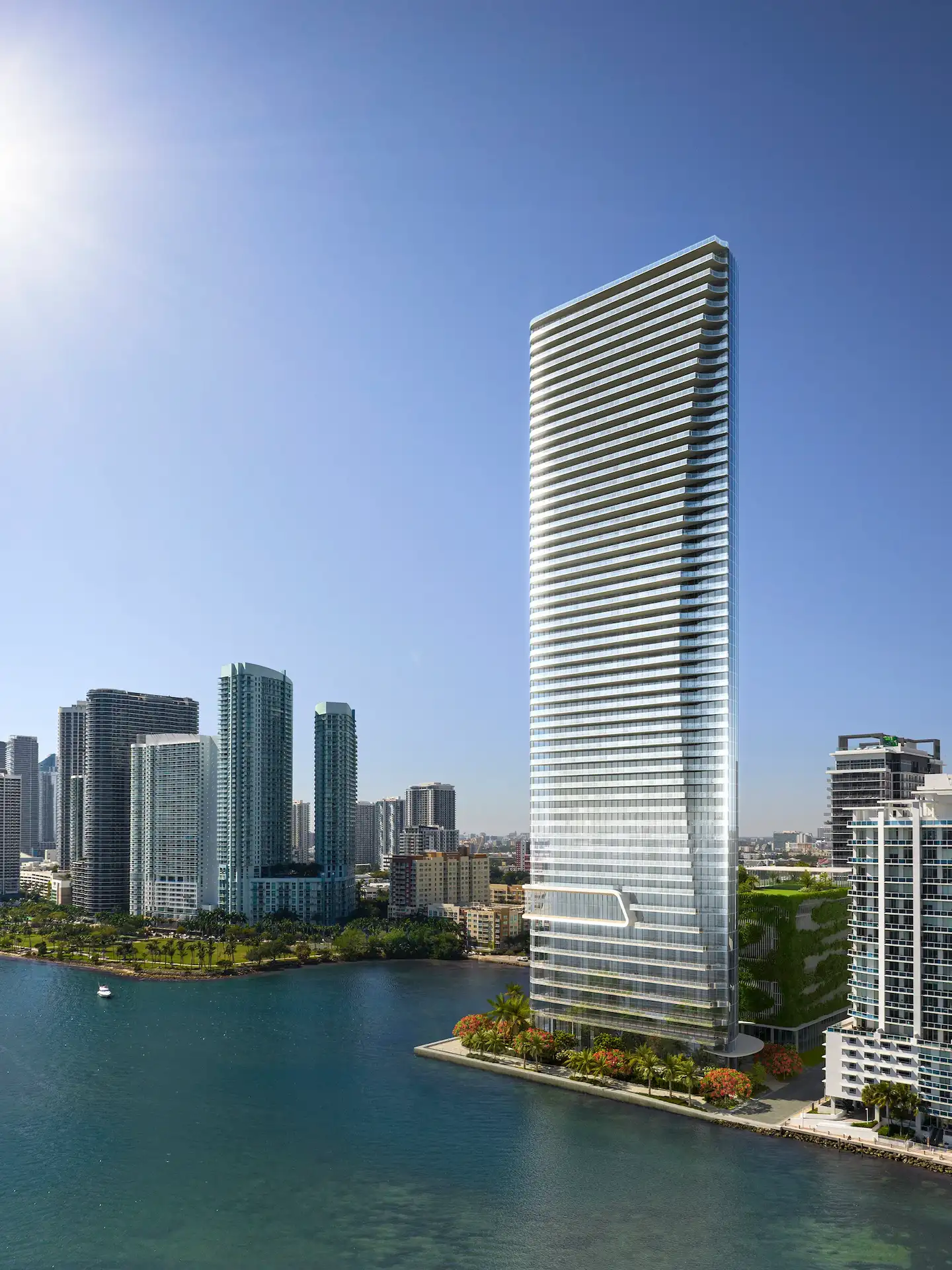 Aerial view of Edition Residences Edgewater, a modern waterfront glass tower in Miami with skyline and bay in background.